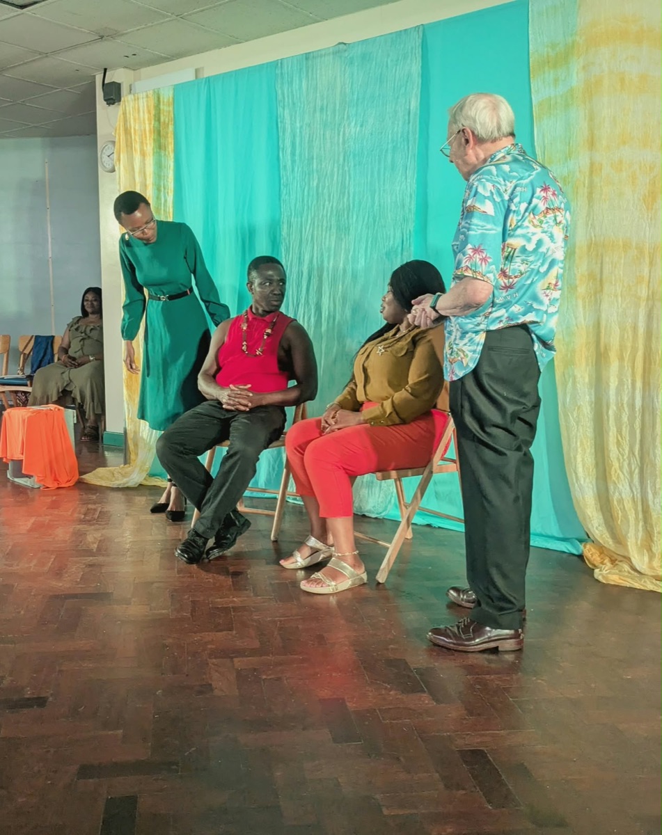 Participants performing a seated scene in front of turquoise and yellow drapes